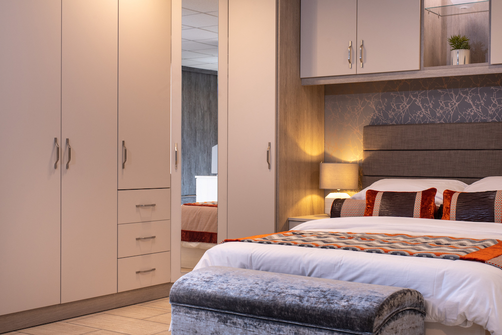 a bedroom with fitter wardrobes, a bed and a bedside table with a lamp on it