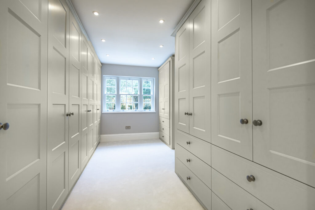 a light and airy walk-in wardrobe with white carpet, white wardrobes and a window.