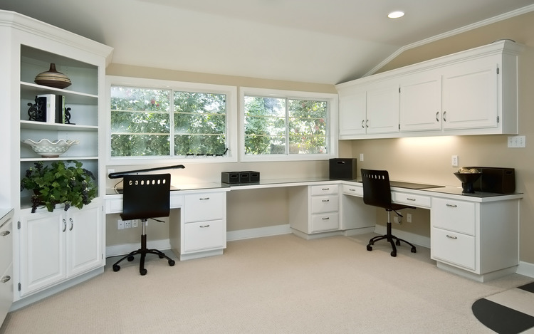 a home office with white desks, white cupboards and two black office chairs.