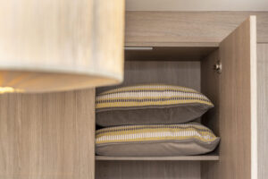 A wardrobe with one door open and two pillows stacked on top of each other on the top shelf.